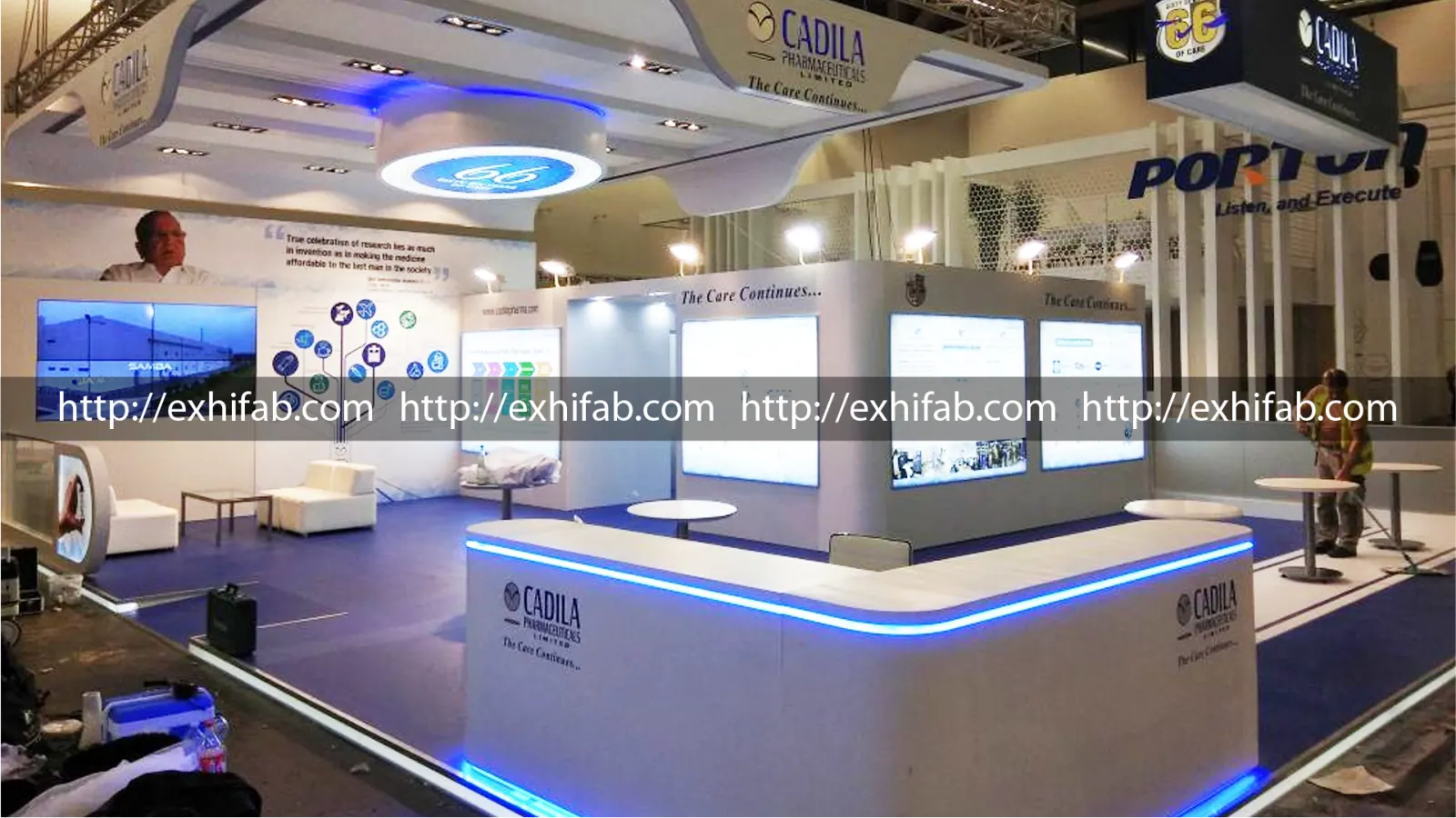 Floor-level view of the Cadila Pharmaceuticals exhibition stand showing the illuminated reception counter and interactive display wall